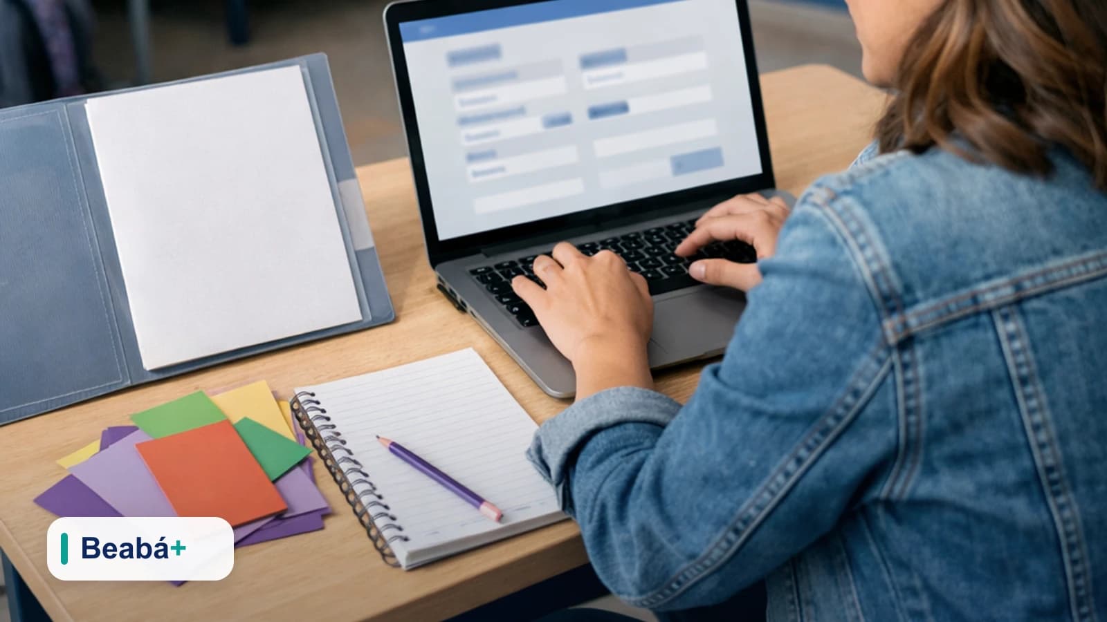 Professora cadastrando e configurando o perfil de um aluno no notebook, em uma mesa com materiais escolares.