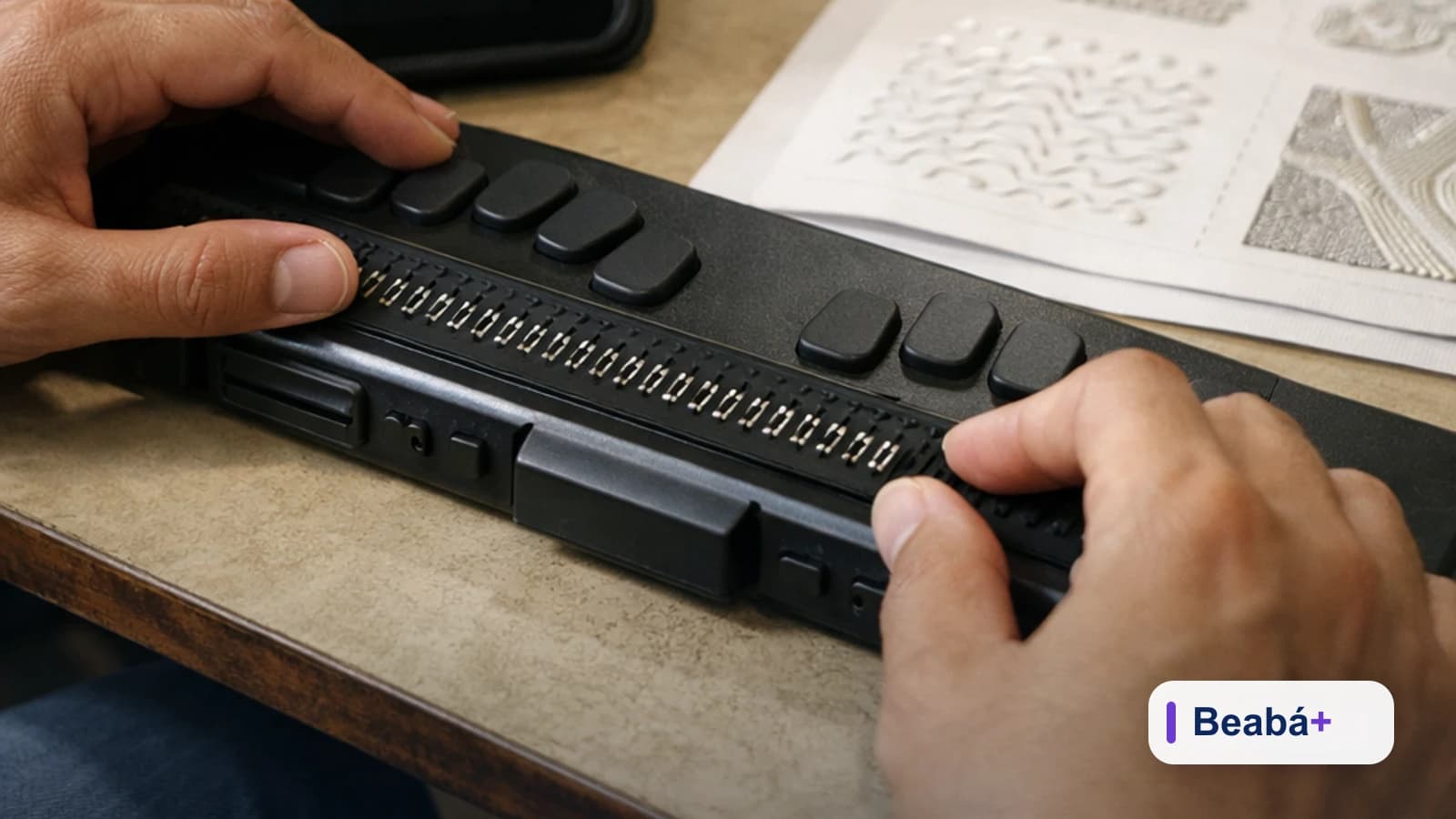 Mãos ajustam uma Linha Braille ao lado de um tablet e materiais de aula.